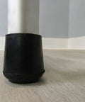 Close-up of Kick The Squeaks 1.5 Inch Round Rubber Chair Leg Caps in black on a hardwood floor protecting against dents.