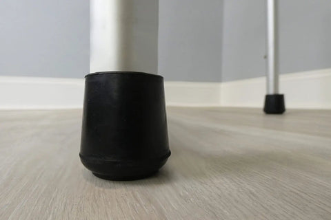 Close-up of Kick The Squeaks 1.5 Inch Round Rubber Chair Leg Caps in black on a hardwood floor protecting against dents.