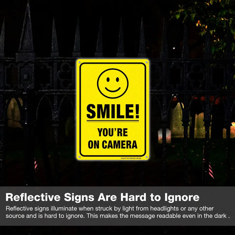 Two Pack Smile You're On Camera Video Surveillance Sign For Home And Business 10x7 aluminum sign on a fence at night.