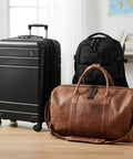Black suitcase, black backpack, and brown leather duffel bag on wooden floor in front of white wall and map.