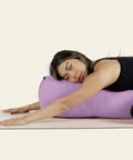Woman resting on purple yoga bolster pillow, Ultra Plush Yoga Bolster Pillow For Restorative Poses And Meditation, Cushioned With Soft PET Fill, 100 Cotton Cover That Is Washable, Built For Deep Stretches And Cozy Pain Free Practice.