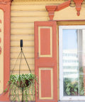 Hanging flower pot on yellow and orange decorative wooden house wall beside a window