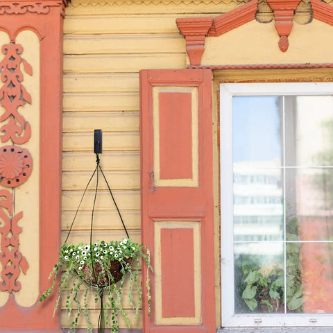 Hanging flower pot on yellow and orange decorative wooden house wall beside a window
