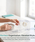 Dual Sided Clear Acrylic Label Roll Dispenser Featuring A Smooth Pull Through Tray on a desk with masking tape.
