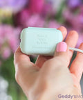Hand holding Kid Friendly USB Charger Cover, Dusty Aqua 3 Pack, Cord Tip Enclosure For Standard USB Cables against floral background.