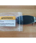 Keychain with warning label on wooden surface, highlighting battery safety instructions.