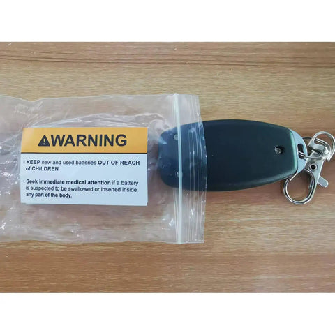 Keychain with warning label on wooden surface, highlighting battery safety instructions.