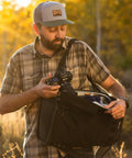 Man accessing gear from ProTactic Lite BP 250 AW III Laptop Backpack With Top And Side Access For A 16 Inch Laptop Exterior Bottle And Tripod Pockets Front Stretch Pocket Rain Cover Great For Pros On The Go Carrying DSLR Mirrorless And Drones 30L