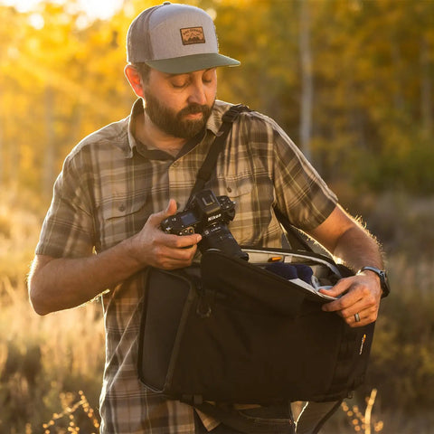 Man accessing gear from ProTactic Lite BP 250 AW III Laptop Backpack With Top And Side Access For A 16 Inch Laptop Exterior Bottle And Tripod Pockets Front Stretch Pocket Rain Cover Great For Pros On The Go Carrying DSLR Mirrorless And Drones 30L