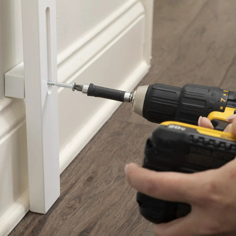 Close-up of installing the Baseboard Gate Adapter For Baby Gates, White Pro Grade Safety Solution, with a drill into a baseboard.