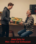 A standing young man giving a gift-wrapped box to a seated older man in a workshop, labeled 'Ideal Gifts for Men/Dad/Car Enthusiast.'