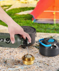 1L Fuel Bottle For Camping And Outdoor Use With Safety Valve pouring fuel into a brass burner, army green canister on rocky surface.