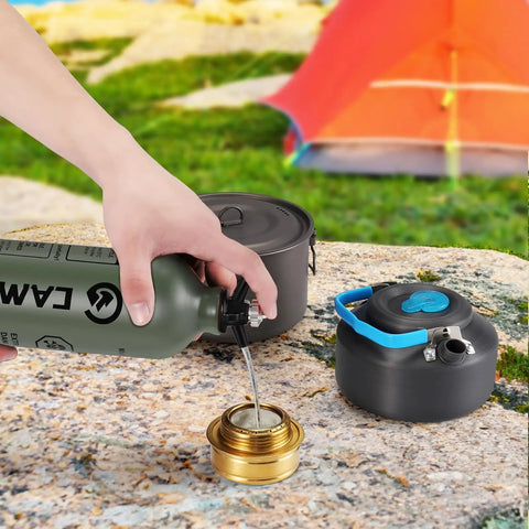 1L Fuel Bottle For Camping And Outdoor Use With Safety Valve pouring fuel into a brass burner, army green canister on rocky surface.