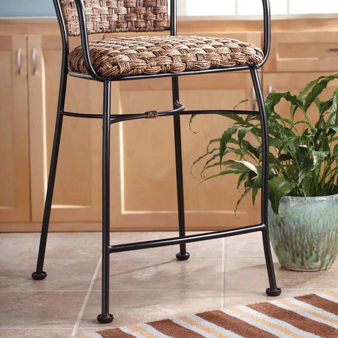 Wicker and metal bar stool on tiled floor with plant and striped rug nearby in a kitchen setting