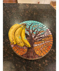 Fifteen Inch Mosaic Tree Of Life Lazy Susan Handcrafted Glass Art Rotating Tray with bananas on brown countertop