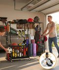 Man using Heavy Duty Rolling Garage Organizer With Wheels For Indoor Sports Gear Storage Including Golf Bags Balls Bats Rackets Skates Mats And More All In One Storage Rack With Basket And Hooks Black Large in garage