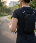 Runner wearing a hydration vest pack with breathable nylon, adjustable chest straps, and multiple pockets on a park path