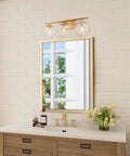 Three Light Gold Vanity Light Fixture With Clear Globe Glass Shades And Slim Taper Arm For Modern Bathroom Decor Exposed Bulbs And Bright Even Illumination With Sleek Gold Finish above mirror.