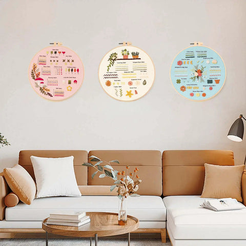 Three embroidery hoops with colorful pre-printed patterns on a living room wall. Beginner Embroidery And Cross Stitch Kit For Adults 3 Pack
