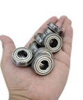 Ten metal precision ball bearings with hex bore held in palm; 1/2 in hex bore, 1-1/8 in OD.
