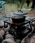 Heavy Duty Dutch Oven Lid Lifter With Coil Handle lifting a hot lid from a cast iron pot over campfire, ideal for outdoor cooking