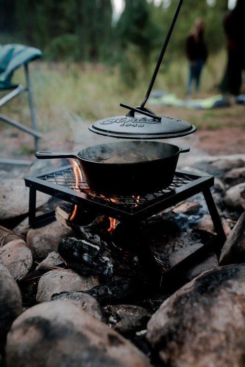 Heavy Duty Dutch Oven Lid Lifter With Coil Handle lifting a hot lid from a cast iron pot over campfire, ideal for outdoor cooking