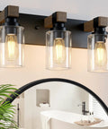 Give Your Mirror Space A Major Glow Up With This Three Bulb Bathroom Vanity Light In Matte Black And Raw Wood Grain Secured By Rock Solid Steel Mounts For Straight Up Rustic Charm, showing clear glass bulbs.