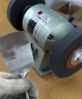Close-up of an 8 inch nylon fiber buffing wheel on a bench grinder with a metal spatula being polished.