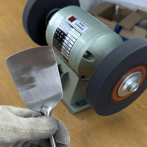 Close-up of an 8 inch nylon fiber buffing wheel on a bench grinder with a metal spatula being polished.