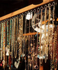 Various necklaces and jewelry hanging from a wooden rack in bright sunlight.