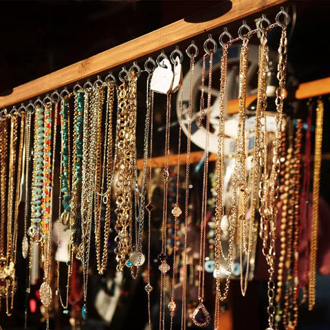 Various necklaces and jewelry hanging from a wooden rack in bright sunlight.