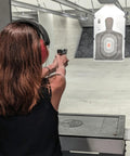 Person firing handgun at shooting range target wearing ear protection