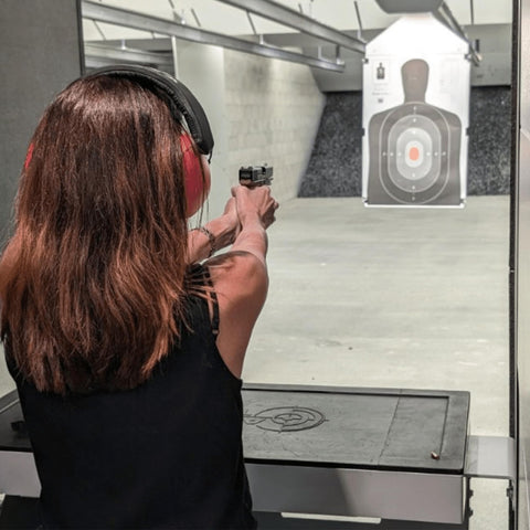 Person firing handgun at shooting range target wearing ear protection