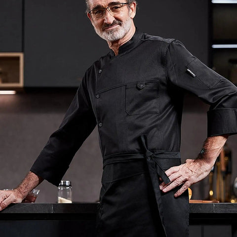 Heavy Duty Chef Coat With Chest And Sleeve Pocket Plus Hella Breathable Fabric That Keeps You Cool In The Heat Top Drawer Restaurant Cook Uniform worn by a chef in a kitchen setting.