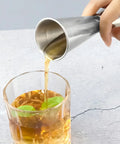 Person pouring liquid using Dual Sided Jigger Set With 1oz And 2oz Markings In 304 Stainless Steel Food Grade Cocktail Measuring Tool For Pros And Home Bars Laser Etched For Precision And Built To Last into a glass with mint leaves.