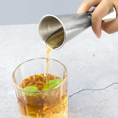 Person pouring liquid using Dual Sided Jigger Set With 1oz And 2oz Markings In 304 Stainless Steel Food Grade Cocktail Measuring Tool For Pros And Home Bars Laser Etched For Precision And Built To Last into a glass with mint leaves.
