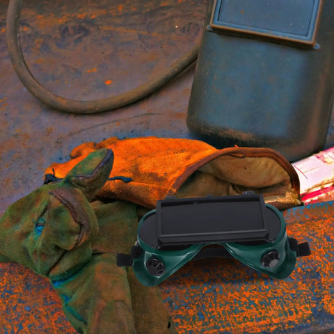 Heavy Duty Welding Goggles With Dual Flip Up Lens placed on work surface with welding gloves and tools in background.
