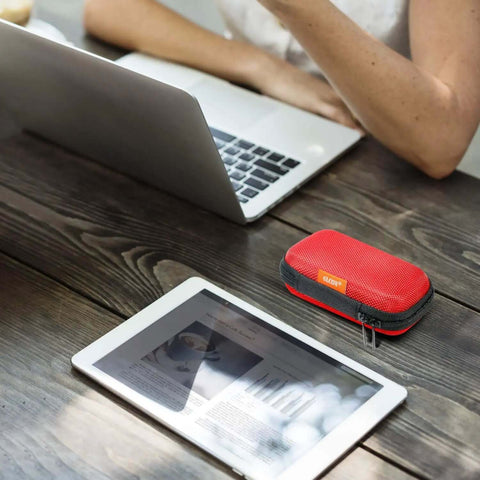Small Red Rectangular Eva Case With Hella Tough Crush Proof Hard Shell And Smooth Zipper Mesh Pouch For Charger Cables Earbuds Memory Cards And Everyday Carry on a wooden desk near a laptop and tablet.