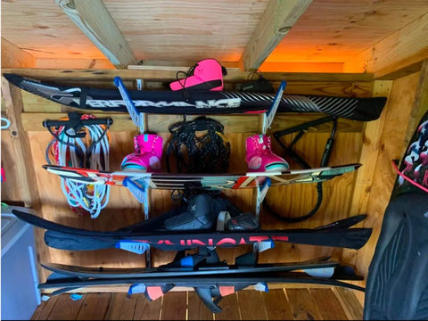 Heavy Duty Multi Level Water Ski Wall Rack Secures Four Pairs Of Skis Wakeboards And Wakesurfers With Scratch Free Padded Arms, organized display of colorful skis and accessories.