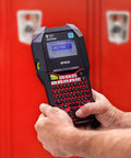 Built Tough Handheld Industrial Label Maker Kit Featuring Slick Rollback Technology And 18Mm Black On White Nylon Tape, held in hand near a red locker.
