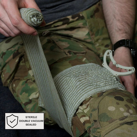 Side view of IFAK Trauma First Aid Kit: gray compression bandage wrapped around leg, camo pants; sterile seal label visible