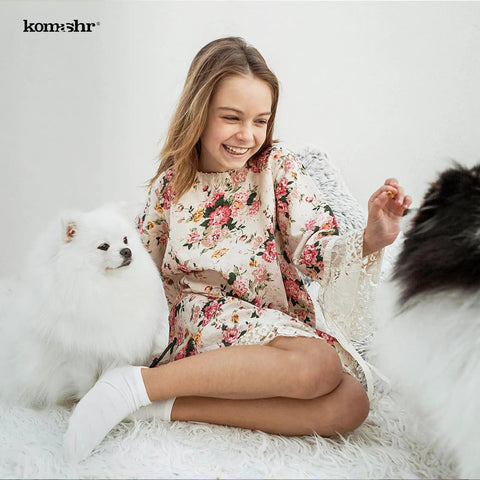 Person in floral dress sitting with two fluffy dogs on a white background