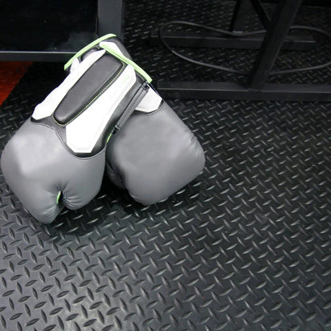 Diamond Plate Rubber Flooring Roll 3 mm Thick 4 Ft By 2 Ft Black Durable Industrial Grippy Floor Mat For Slippery Surfaces Outdoor Walkways And Equipment Protection with boxing gloves on top.