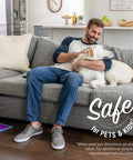 Man sitting on a couch with a dog, Click N Clean Multi Surface Spray Mop visible on the floor near him.