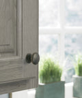 Close-up of Ravino Oil Rubbed Bronze Cabinet Knob, One And A Quarter Inch Diameter on light wood cabinet door