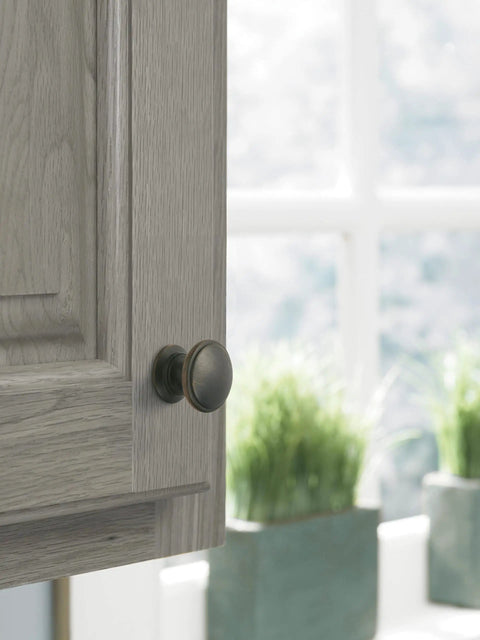 Close-up of Ravino Oil Rubbed Bronze Cabinet Knob, One And A Quarter Inch Diameter on light wood cabinet door