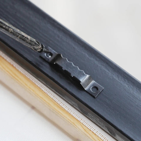 Close-up of Top Shelf Heavy Duty Black Sawtooth Picture Hangers attached to wood frame, supports 20 lbs.