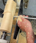 Close-up of a carbide wood-turning tool with a color-coded 12-inch aluminum lathe handle shaping a light wood blank on a lathe.
