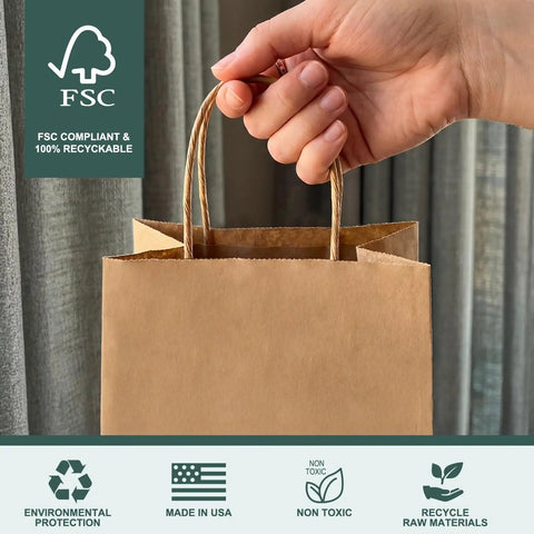 Hand holding a small brown kraft gift bag with handles, FSC compliant, includes environmental icons, made in USA, 5.25x3.75x8 inches.