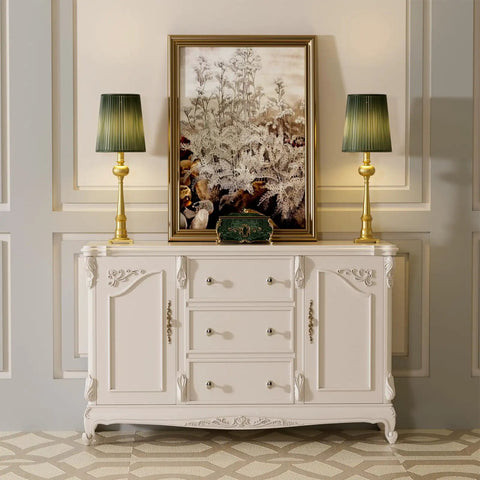 White sideboard with drawers, decorative molding, gold lamps, and framed artwork on panel wall